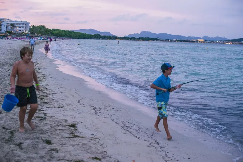 Strand an der Bucht von Alcúdia mit Bergen und Angler am Abend Strand an der Bucht von Alcúdia mit Bergen und Angler am Abend