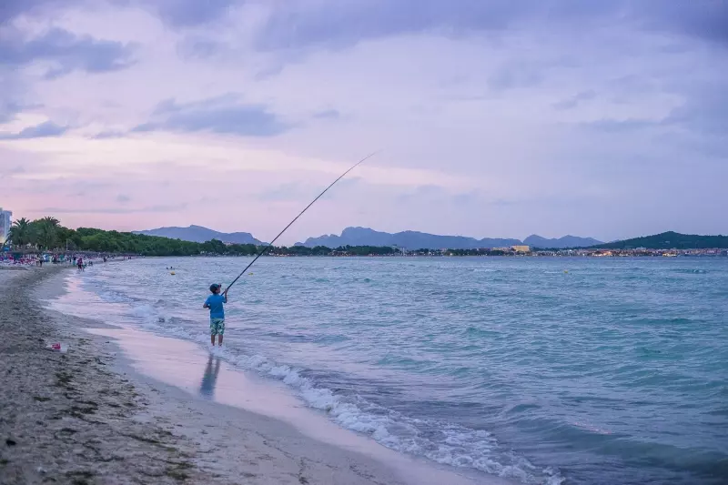Angler am Strand von Mallorca bei ruhigem Meer und Bergkulisse
