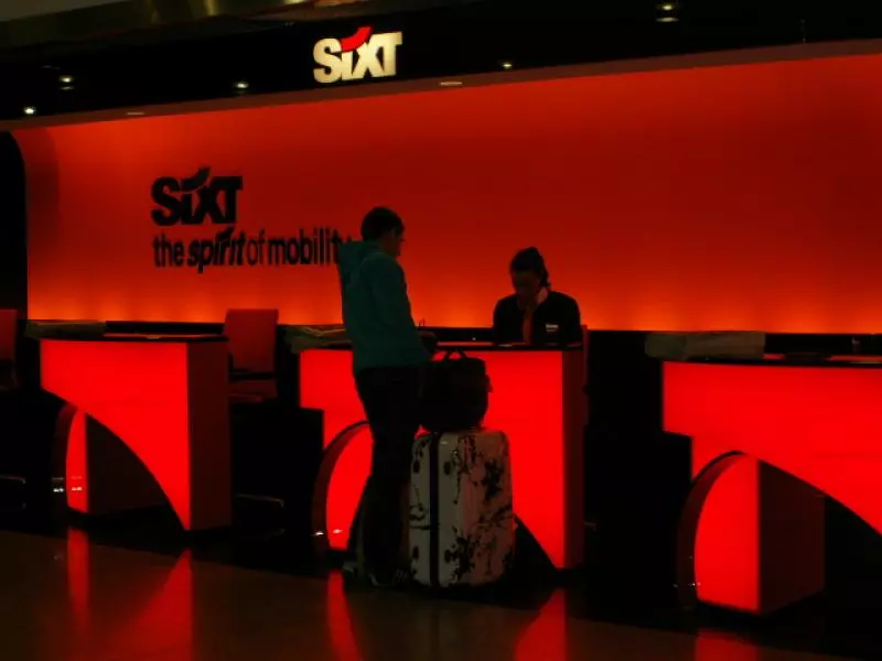 Mietwagenschalter am Flughafen mit roter Sixt-Ausgabe und Reisenden
